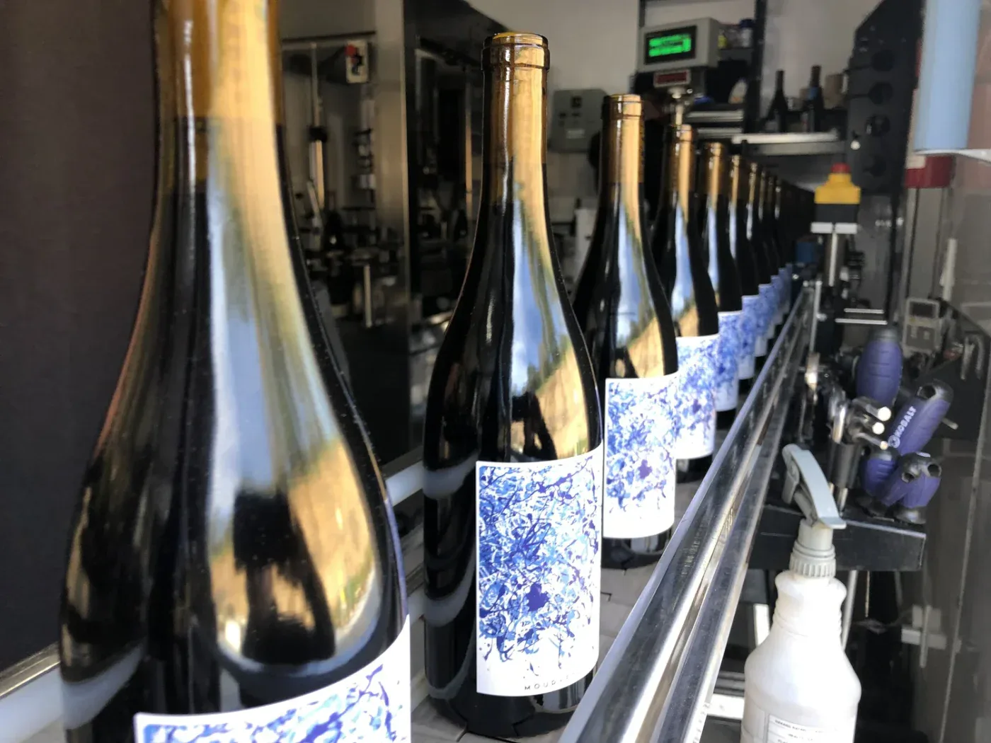 Bottles of wine labeled "Benevolent Neglect" on a production line in a winery setting.